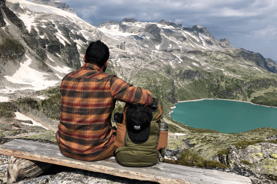 A man with a backpack sitting in the mountains watching a lake.